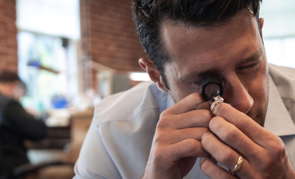 Man using a magnifying glass to inspect the quality of a diamond baguette ring.