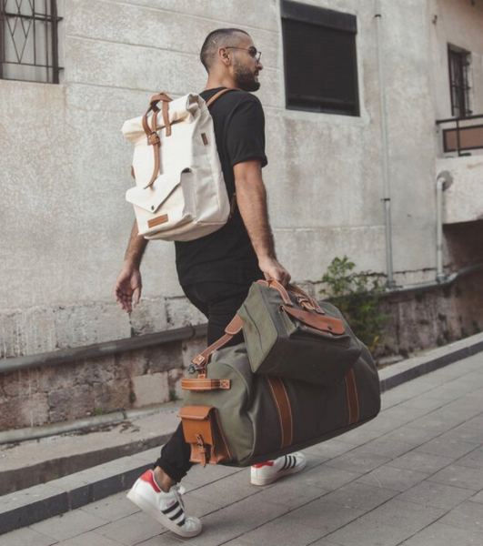 a man with glasses holding a hipster backpack and a bag