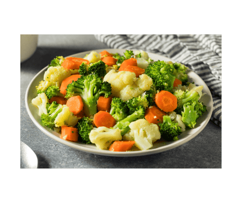 A plate of steamed broccoli, cauliflower, and carrots on a grey countertop with a dish towel and a spoon