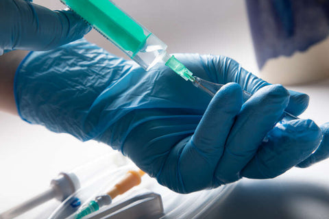 A gloved hand holding a syringe with green liquid