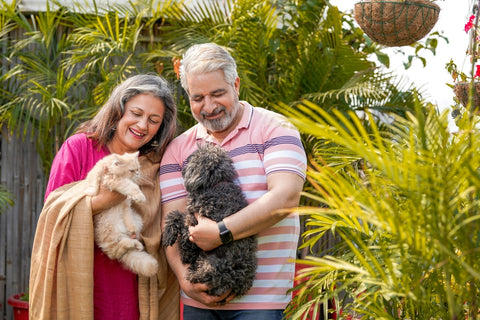 Two people holding cats in a garden with blurred faces and various plants