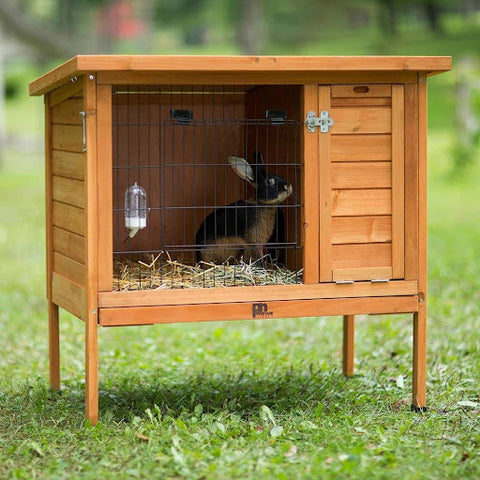 A wooden rabbit hutch with a black rabbit on a grassy lawn.