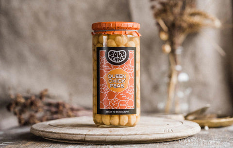 Image of Bold Bean co Queen Chickpeas. It is a tall, glass jar sitting on a wooden table.