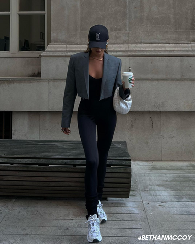 Female influencer in black jumpsuit and grey blazer holding coffee