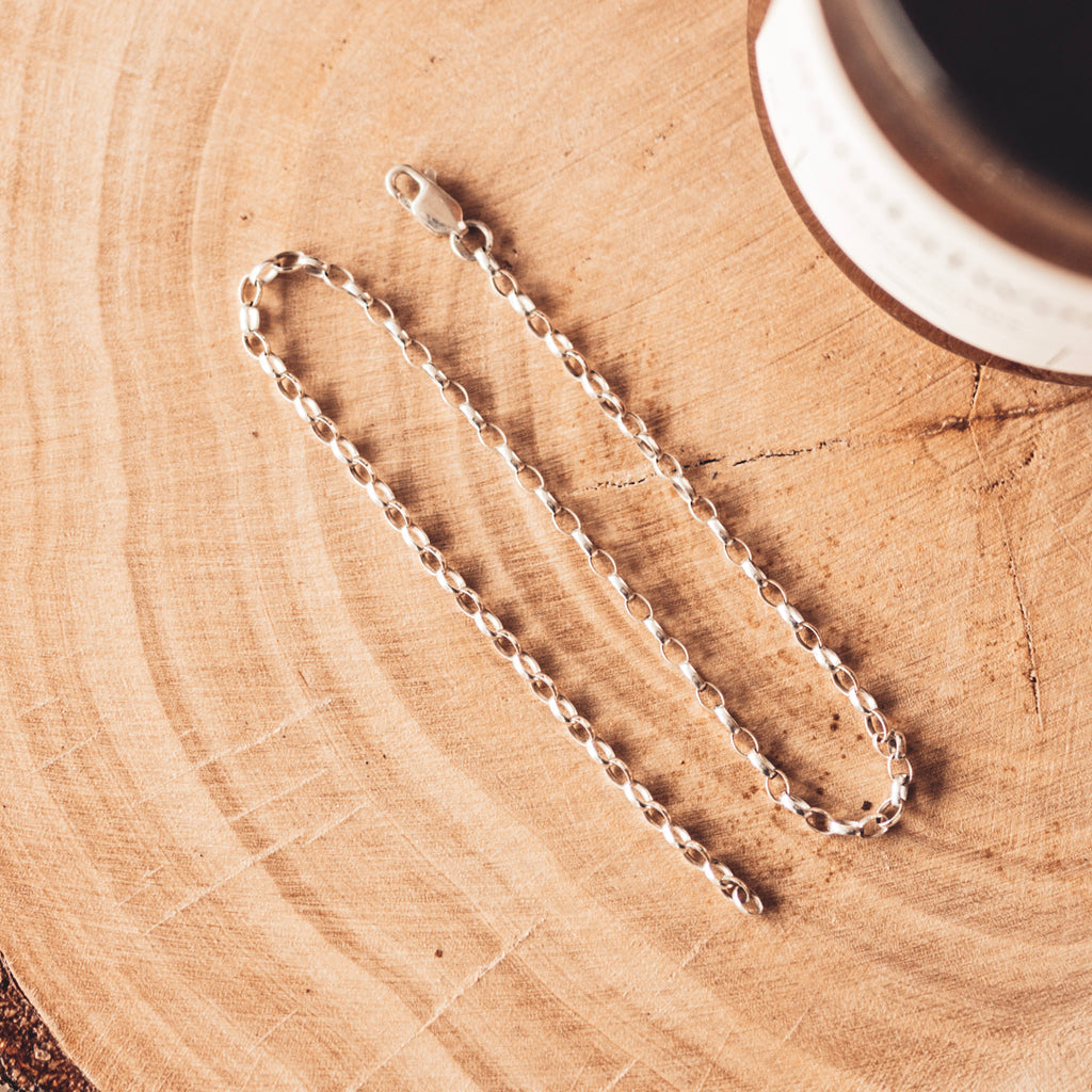 Srebrny łańcuszek o splocie rolo leżący na drewnianej podstawce. 