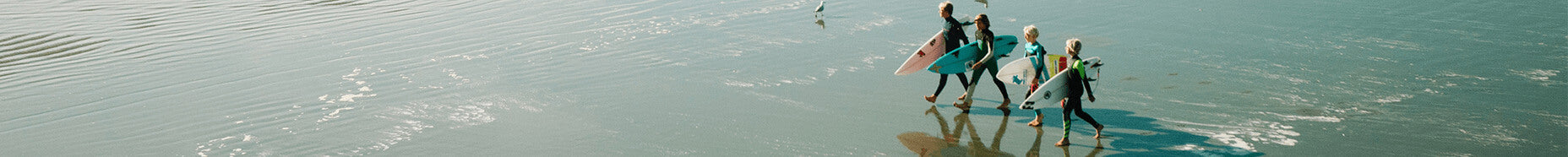 kids in wetsuits on the beach carrying surfboards