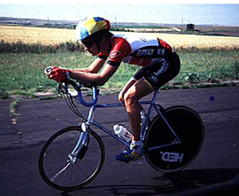 A time trial cyclist rides his bike on a road in a racing position