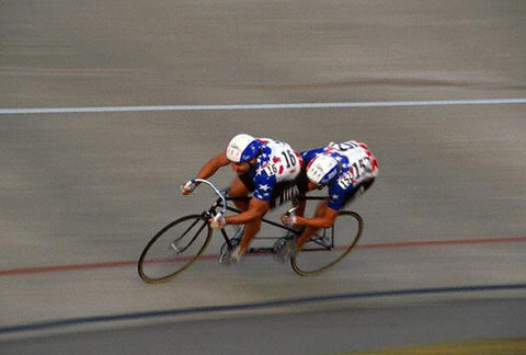 Paul Swift rides with another cyclist on a tandem track bike around a curve