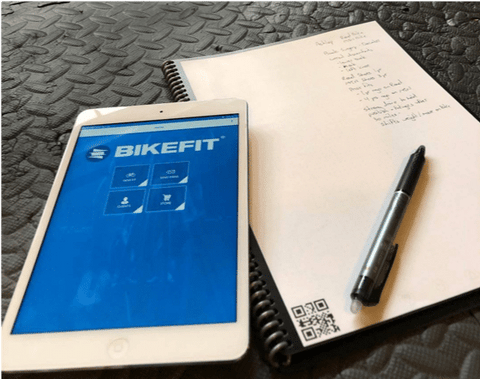 Phone with BikeFit app open on top of a notepad with measurements