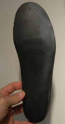 A cycling shoe insole is being held up and there is visible wear towards the outside edge