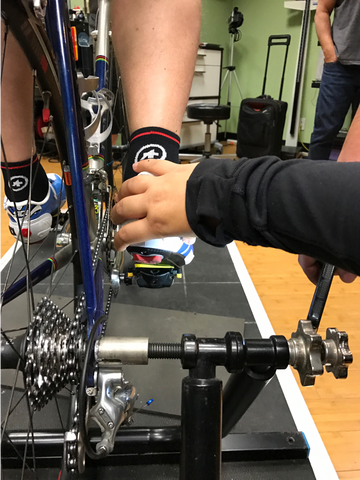 A bike fitter adjusts a cyclists heel while they are being fitted on a bike.