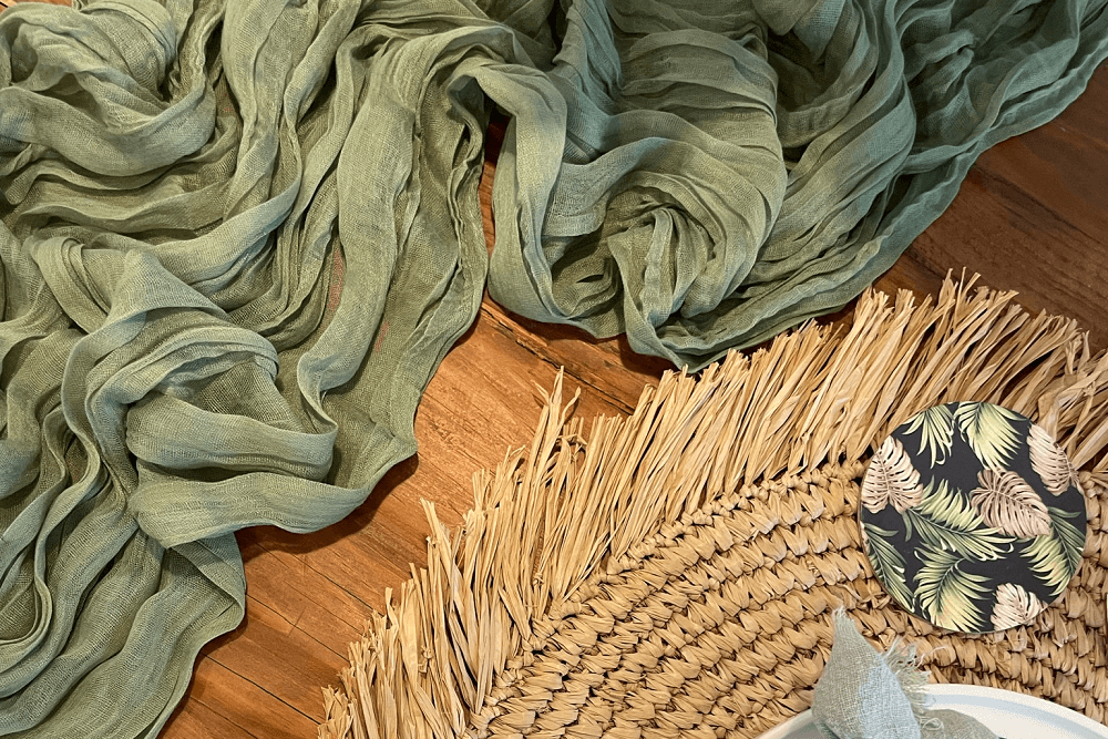 sage green gauze table runner and a raffia placemat on a wooden table