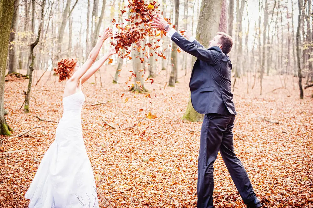 A newlywed couple playing with dried leaves in their autumn wedding