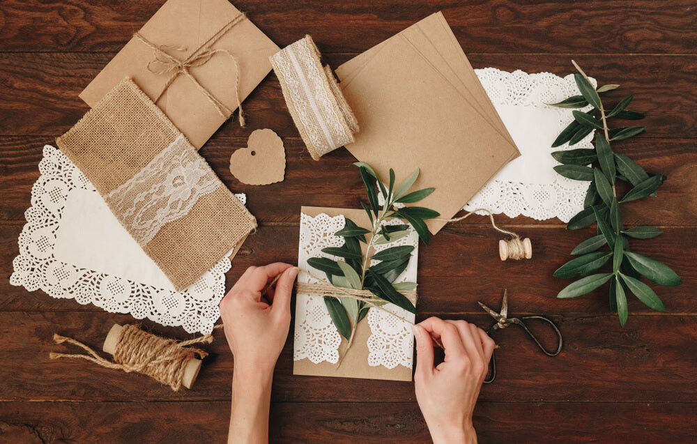 top view of DIY rustic wedding invitations with lace, linen, greenery, and twine details