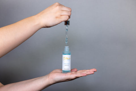 Ethos Skincare HA Blue Serum resting on a woman’s palm, with the dropper being lifted out of the bottle.