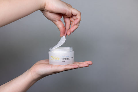 Ethos Skincare Kojic Pads resting on a woman’s palm, with one pad being lifted out of the container. 