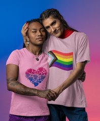 Picture of a couple. Both are people of colour. The one on the left is wearing a pink tshirt with a bisexual heart of hearts pattern on the front. The one on the right is wearing a pink tshirt with a waving rainbow progress flag on the front.