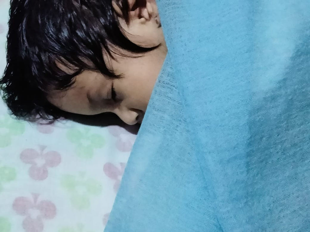 A toddler sleeping on a bed with an ultralight felted cashmere scarf as a blanket.