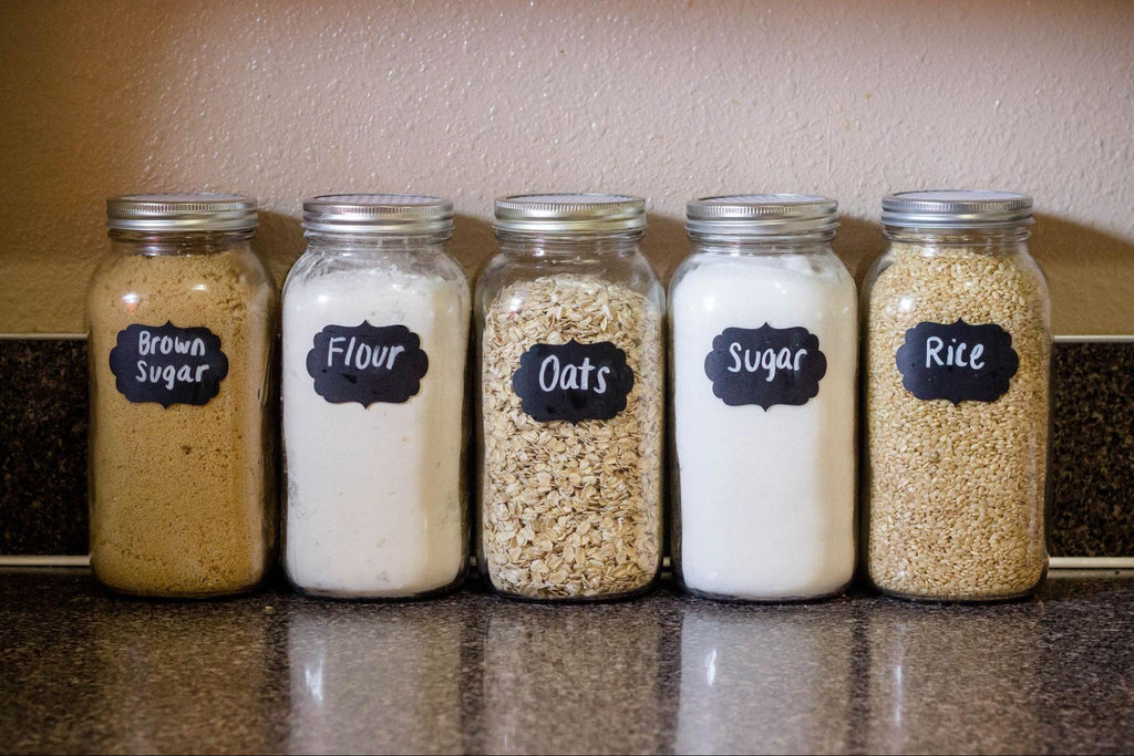 Pantry baking ingredients in jars lined up in a row on a countertop.