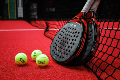Wilson padel racquets and balls on a red court.