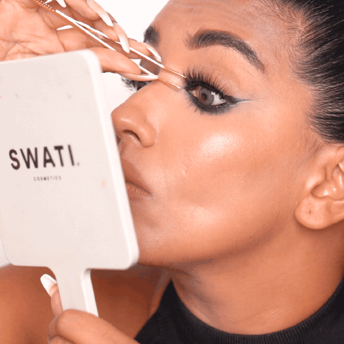 Swati Verma usa el espejo de maquillaje para aplicar el rímel con un aplicador de pestañas de doble punta.