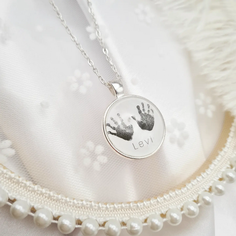 Silver necklace and pendant with personalised handprints set in glass on decorative background