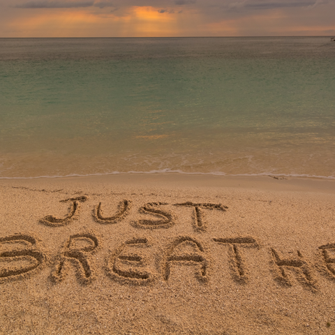 "just breathe" written in the sand by the sea