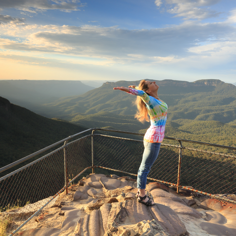 woman standing on a cliff edge with mountains behind her, being in nature to cope with hair loss