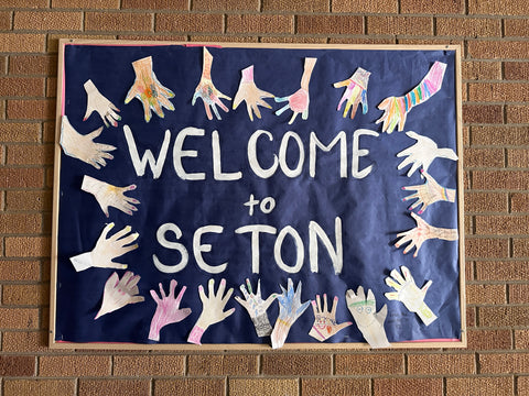 A poster that says "welcome to seton" with cut out children's handprints