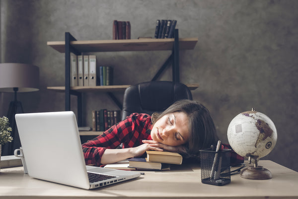 Woman sleeping at her desk with a macbook and books