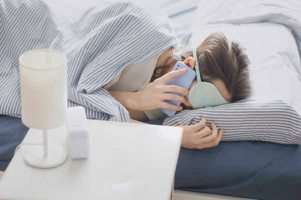 Woman in bed using a smartphone and wearing a sleeping mask