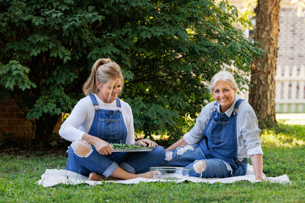 Leah and Sandy sitting on a blanket outside smiling. Leah is holding a tray of green beans.
