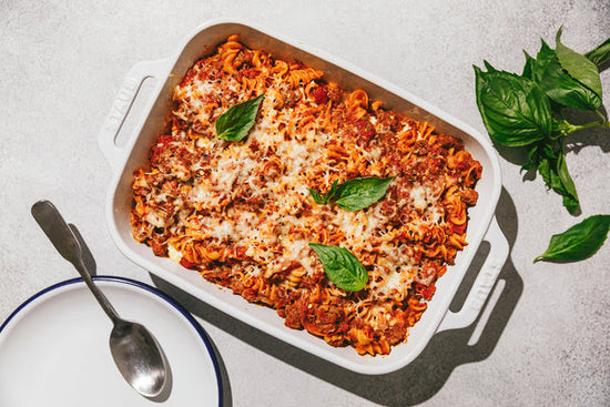 A high protein pasta bake made with lupin pasta in a white casserole dish with fresh basil.