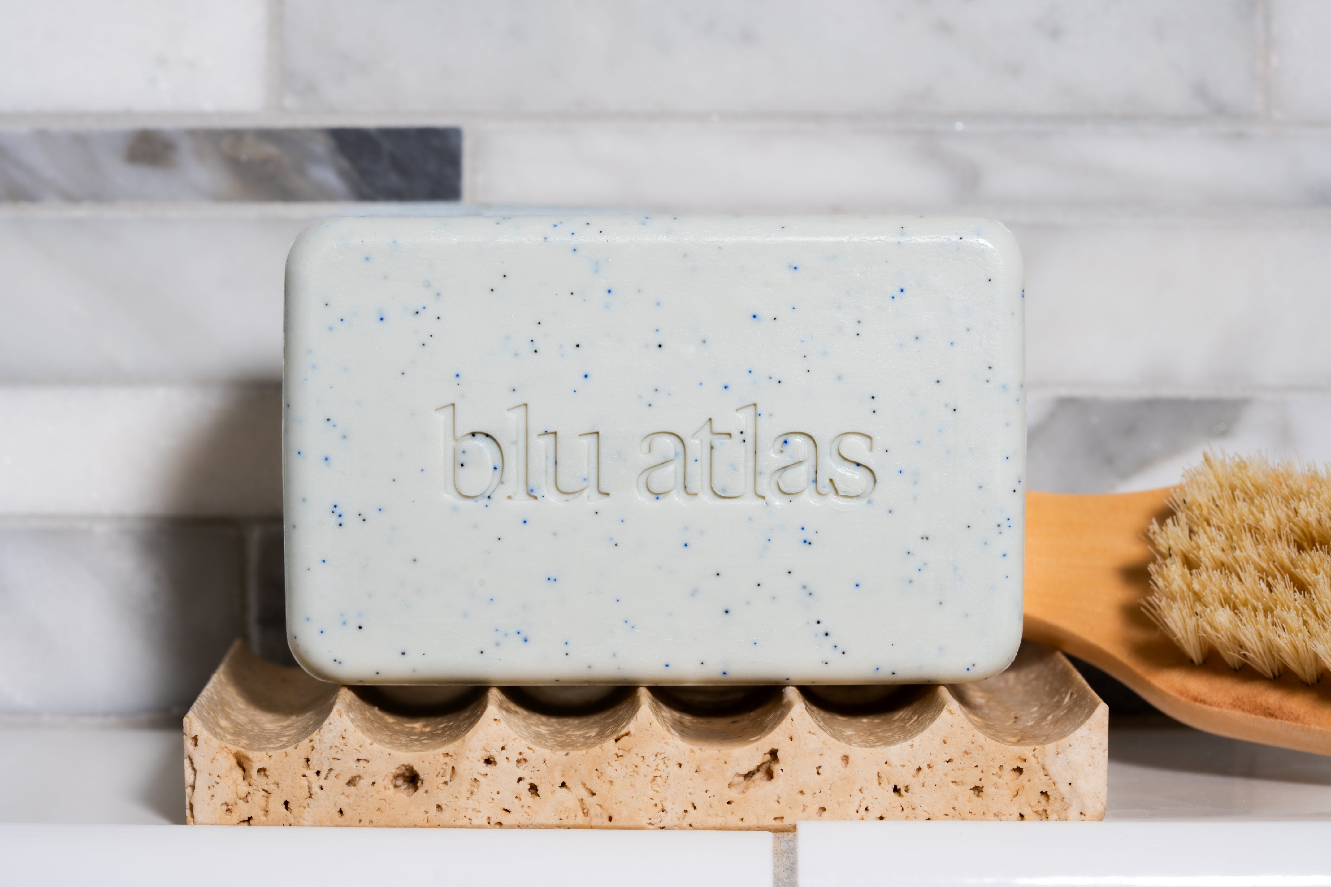 A speckled soap bar embossed with 'blu atlas' rests on a stone holder.