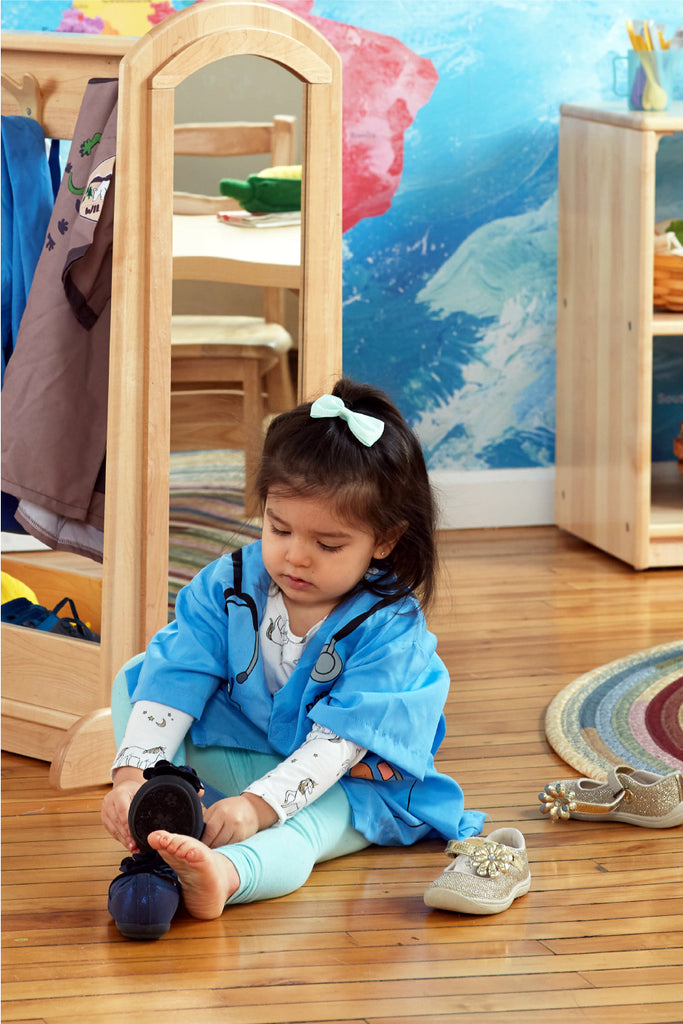 Imagen de una niña en edad preescolar vistiéndose con un disfraz de juego de simulación de un centro de disfraces de Guidecraft.
