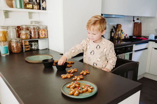 Young boy reaching for gingerbread cookies, standing in Kitchen Helper at kitchen countertop