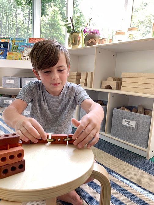 Image of school-aged boy in a homeschool environment using Guidecraft Little Bricks educational toy set. 