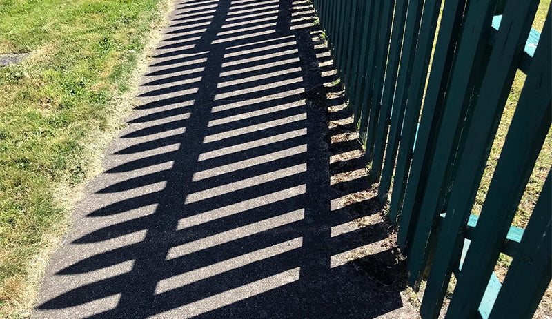 Shadows cast onto the road by a fence