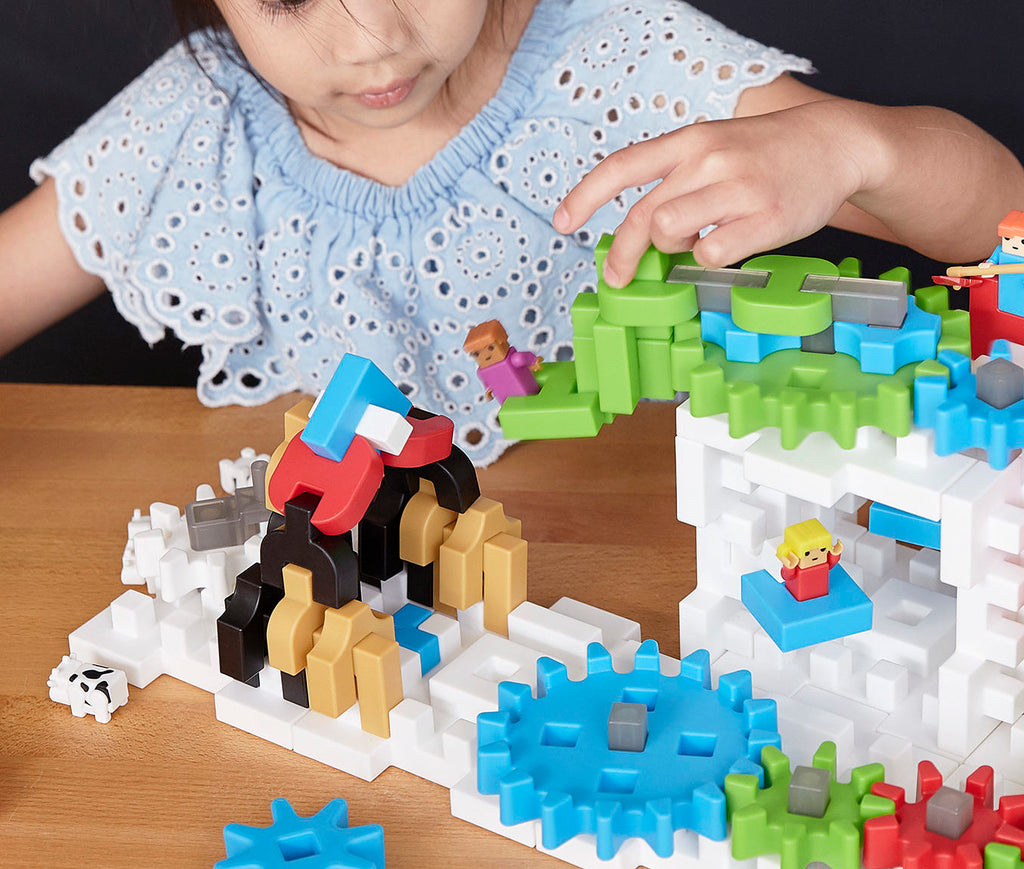 Imagen de una niña jugando con Guidecraft IO Blocks, un juguete STEM para niños que presenta engranajes, piezas de conexión, personas IO y vacas para experiencias de construcción de juegos imaginarios.