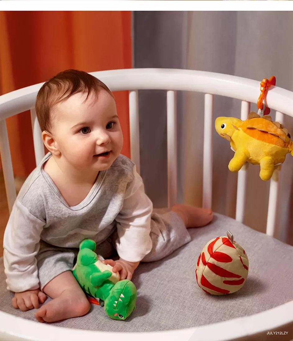 A baby in a stroller playing with a plush dinosaur toy