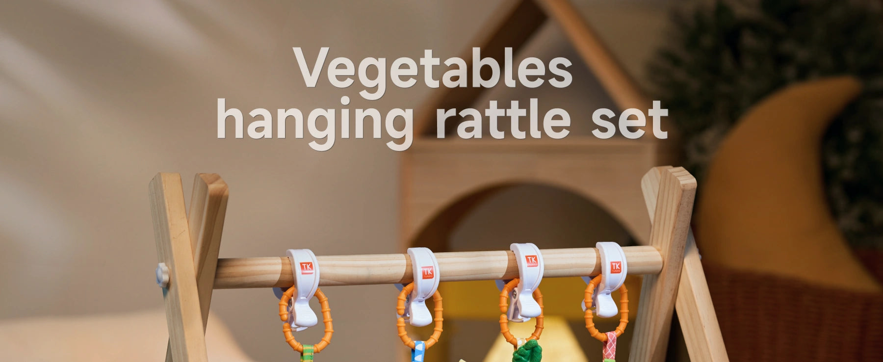 A wooden play gym bar with vegetable-themed hanging rattle toys clipped securely using orange and white clips, designed for versatile use on baby gear.