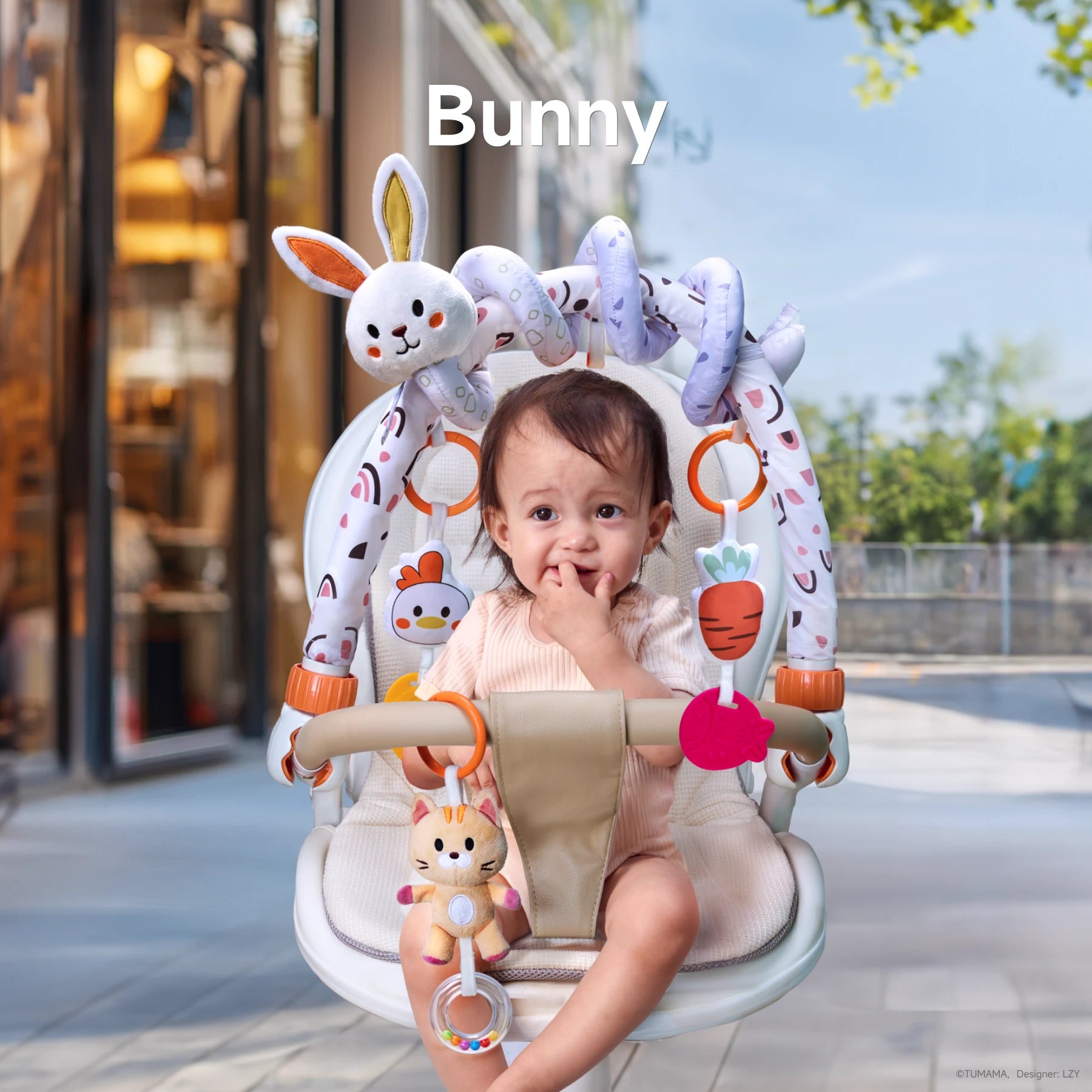 Baby sitting in a stroller with a bunny-themed toy arch, featuring plush animals, carrot-shaped teethers, and colorful hanging toys for infant playtime.