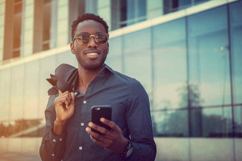 Man in button up shirt wearing sunglasses holding a smartphone