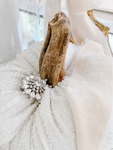 A white fabric pumpkin adorned with a vintage rhinestone brooch