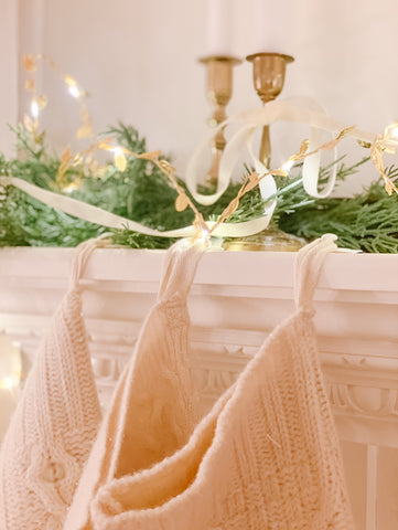 Fairy lights and ivory cable knit stockings hanging from a fireplace mantle