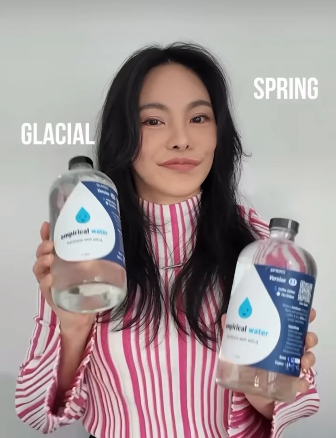 Person holding two bottles of empirical water with labels 'GLACIAL' and 'SPRING.'