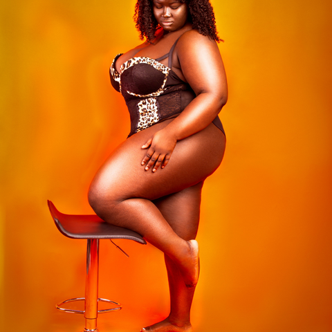 orange background with woman wearing black bodysuit with leopard print trim left knee resting on stool