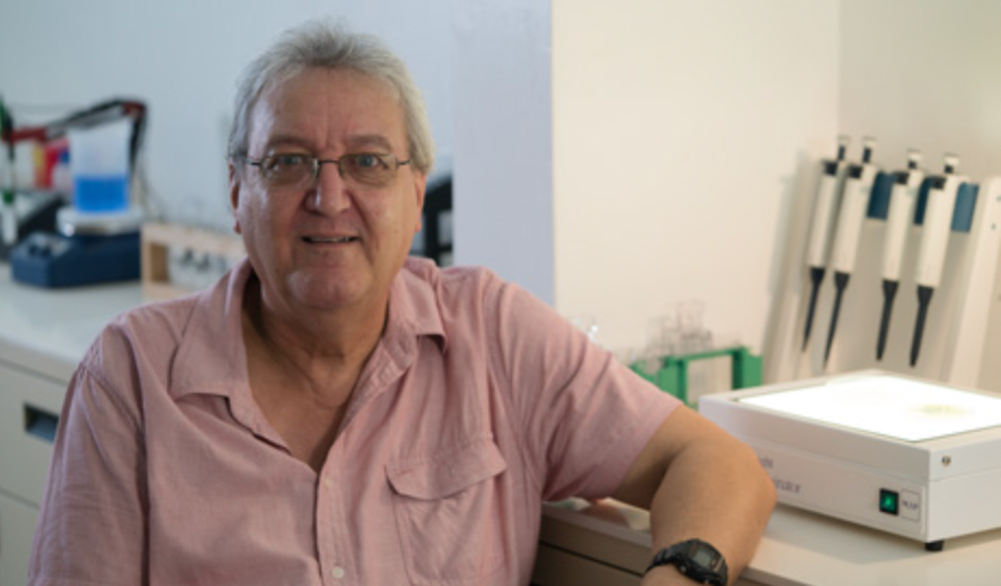 Picture of Professor Dr. Bruce Davidson. He is a white man with glasses and a salmon colored shirt, sitting in a chair in a medical laboratory.