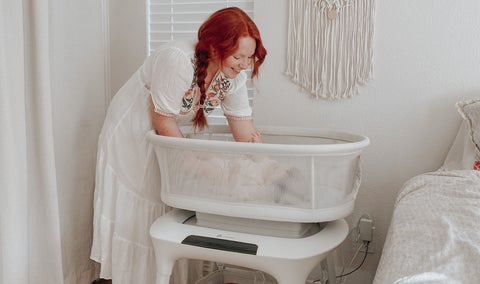 Mother placing baby in the MamaRoo Sleep Bassinet