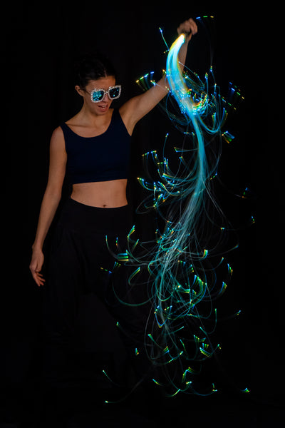 An excited woman holding up a fiberoptic whip, which has brilliant dots of light forming gentle curves towards the ground